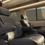 Interior of a passenger van with rows of dark leather captain's chairs, armrests, and ambient overhead lighting